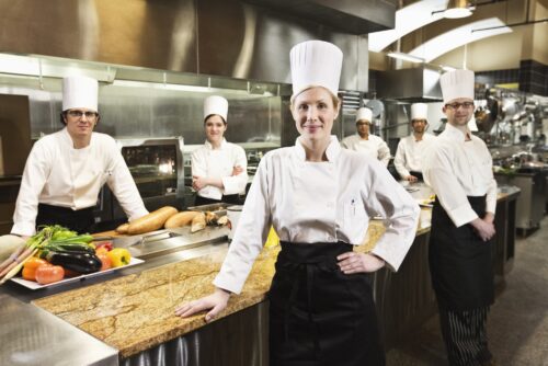 A portrait of a caucasian female chef and her team of chefs in the backgroiund.